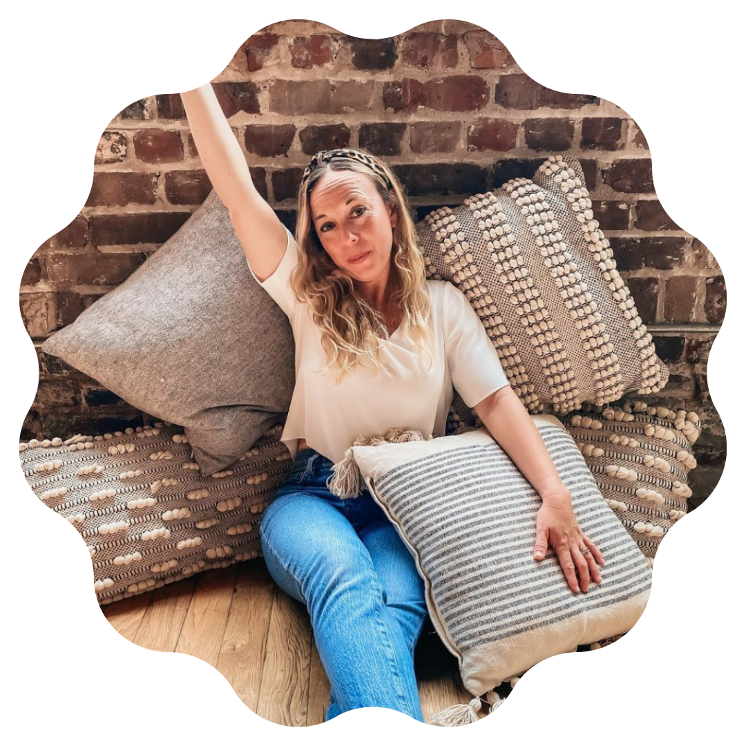 woman sitting on the floor surrounded by pillows with her hands thrown up in the air