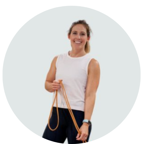 Woman wearing a white tank top and black pants with her hair pulled back in a pony tail, smiling at the camera