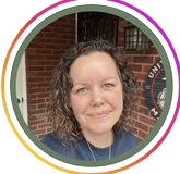 woman wearing a blue shirt sitting outside in front of a brick wall, smiling