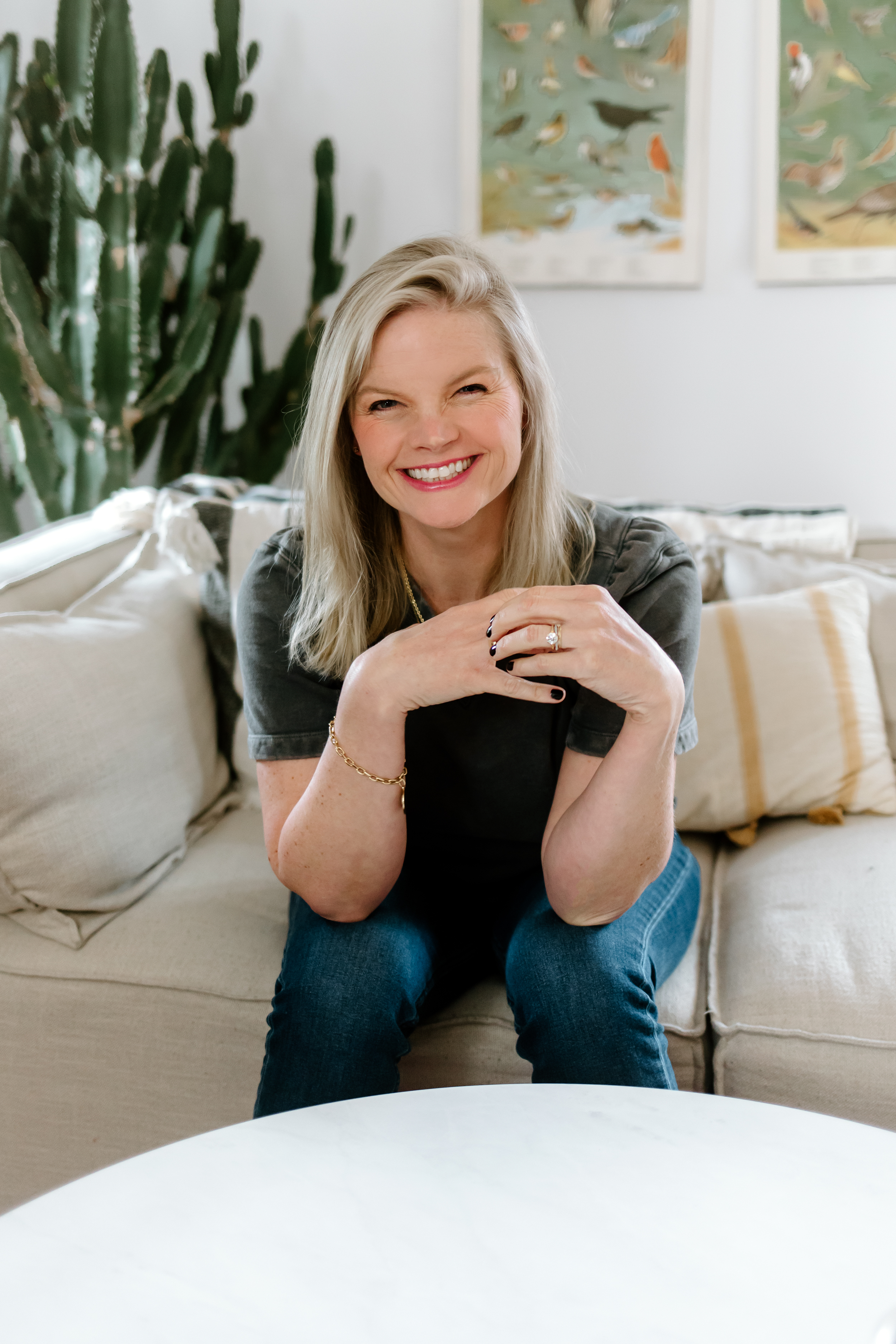 Em wearing a grey shirt sitting on a couch smiling at the camera