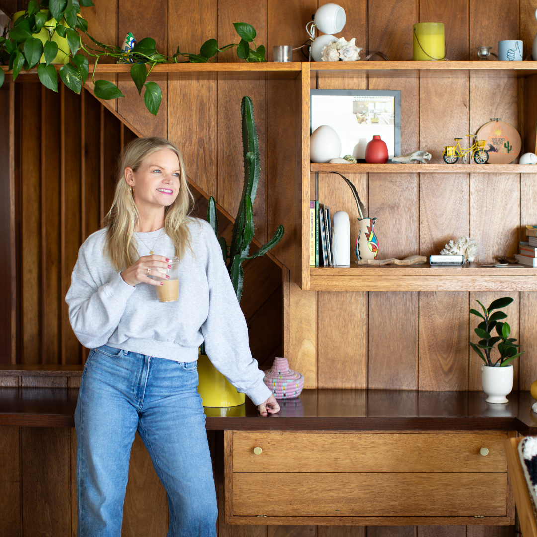 Em smirking and gazing off to the side looking out of a window, wearing a grey shirt with ruffled sleeves