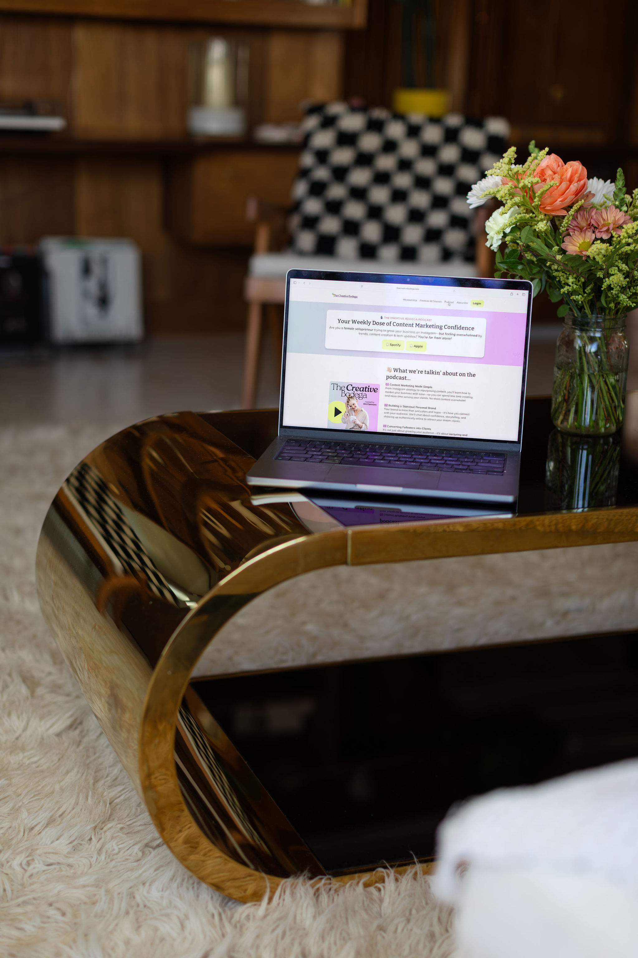 Em's laptop with podcast landing page pulled up on top of a sleek retro gold coffee table and a cream shag rug