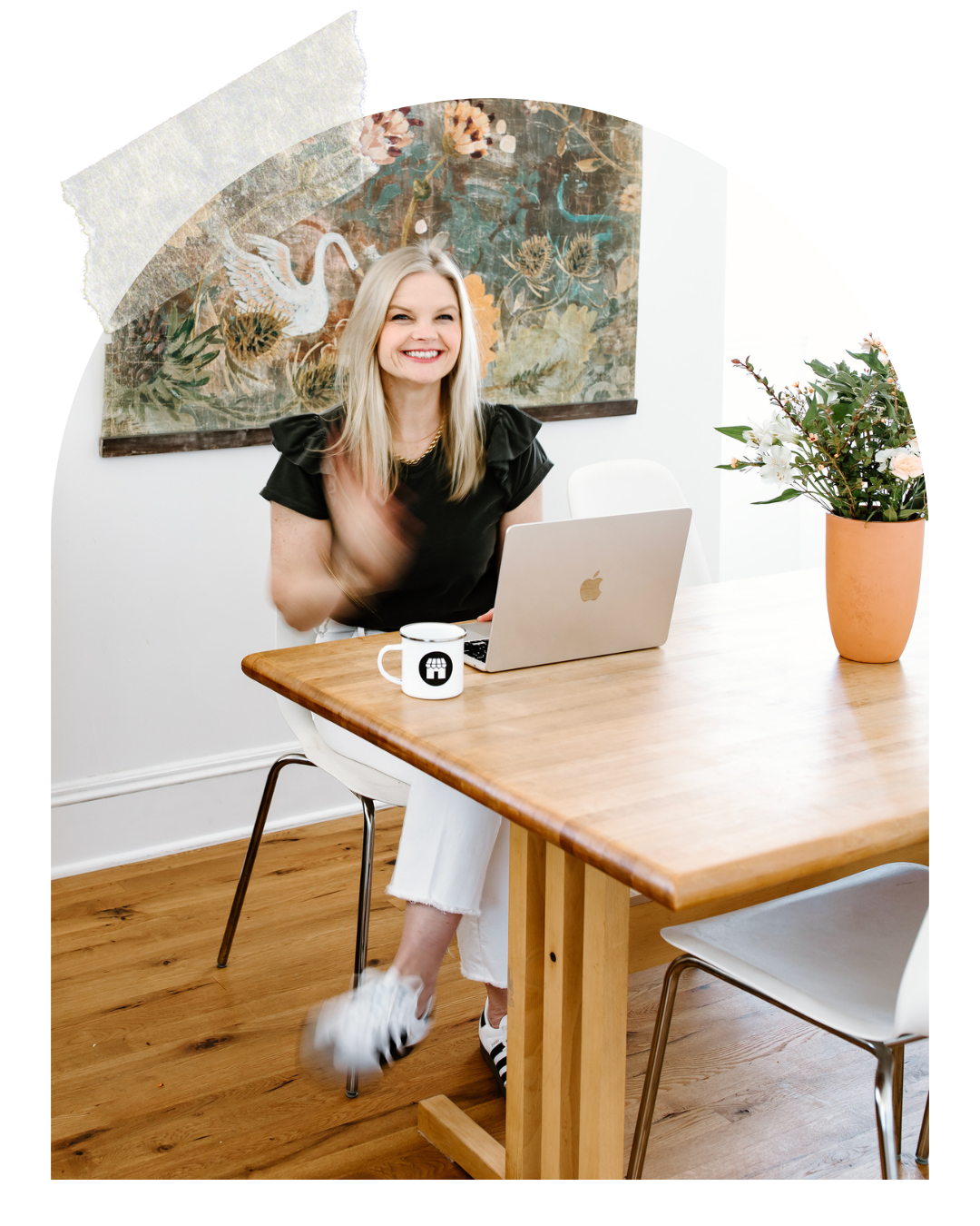 Em sitting behind her laptop smiling at the camera, with her coffee mug next to her and a pot of flowers on her other side
