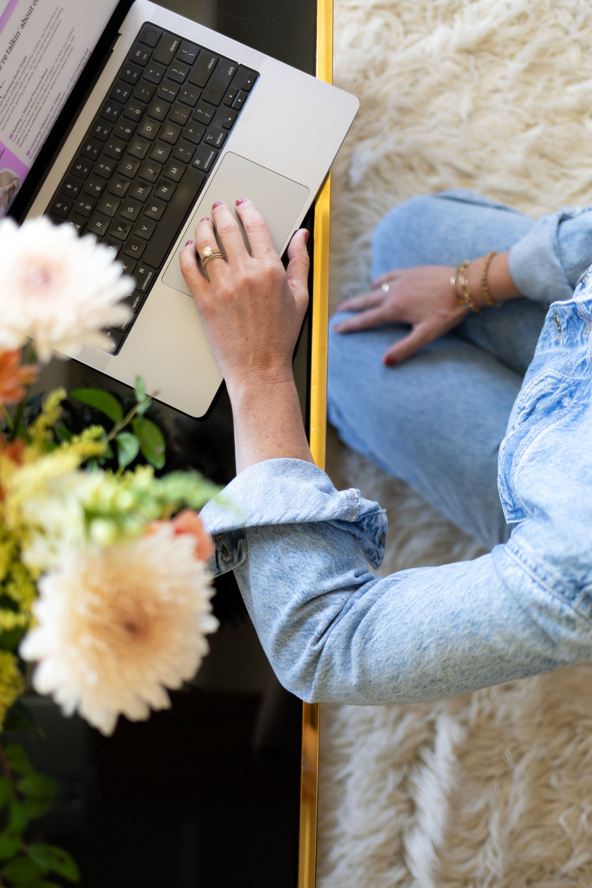 Em's arm in a denim jumper hand hovering over her keyboard with pale pink flowers in a vase