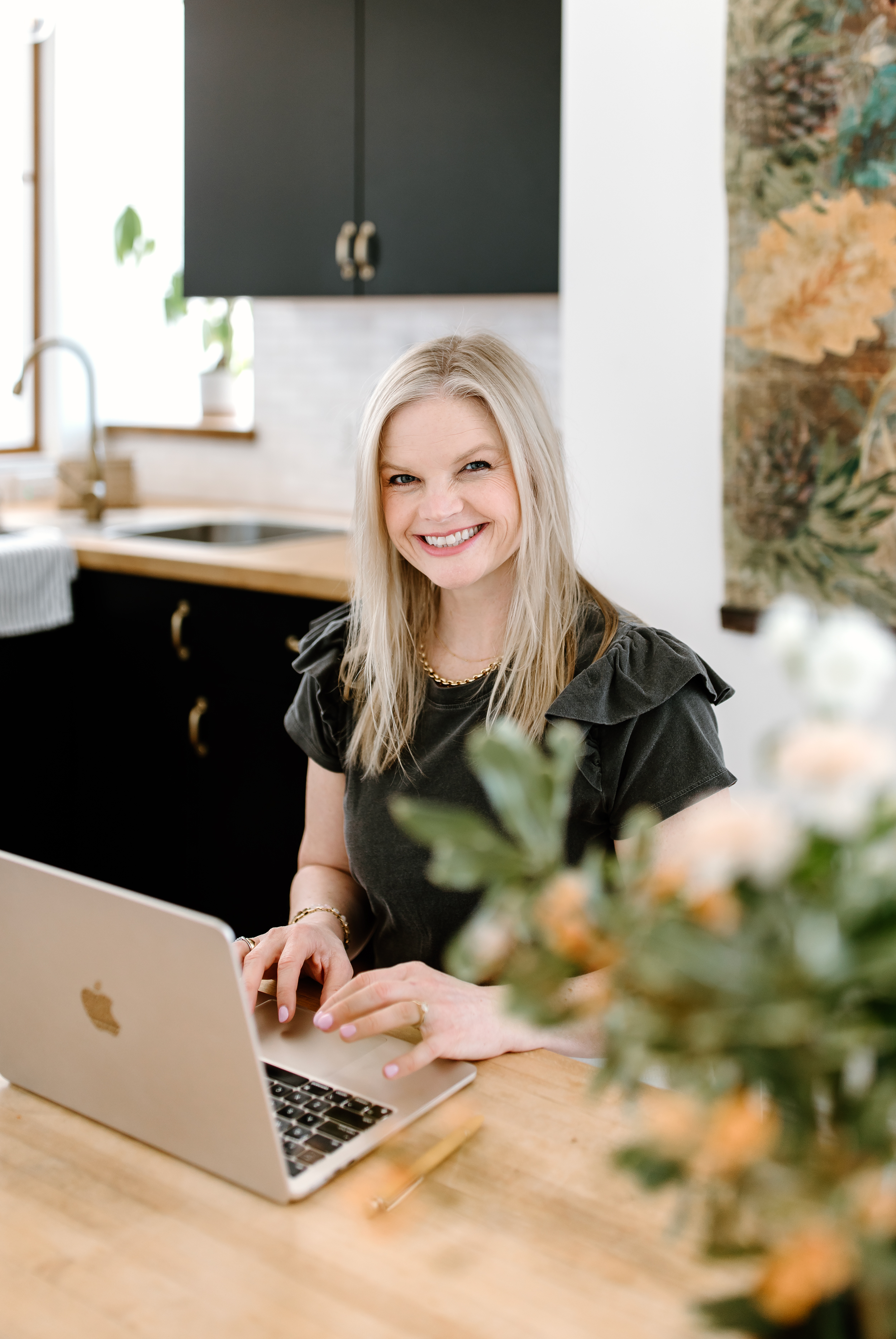 Em wearing a grey t shirt with ruffled sleeves, typing on her laptop