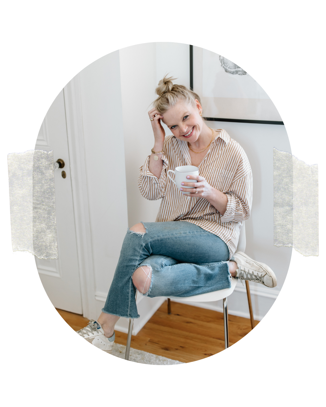 Em wearing a striped button down shirt and distressed jeans holding her coffee mug and smiling at the camera