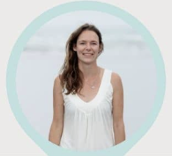woman wearing a white tank top outside at the beach smiling at the camera