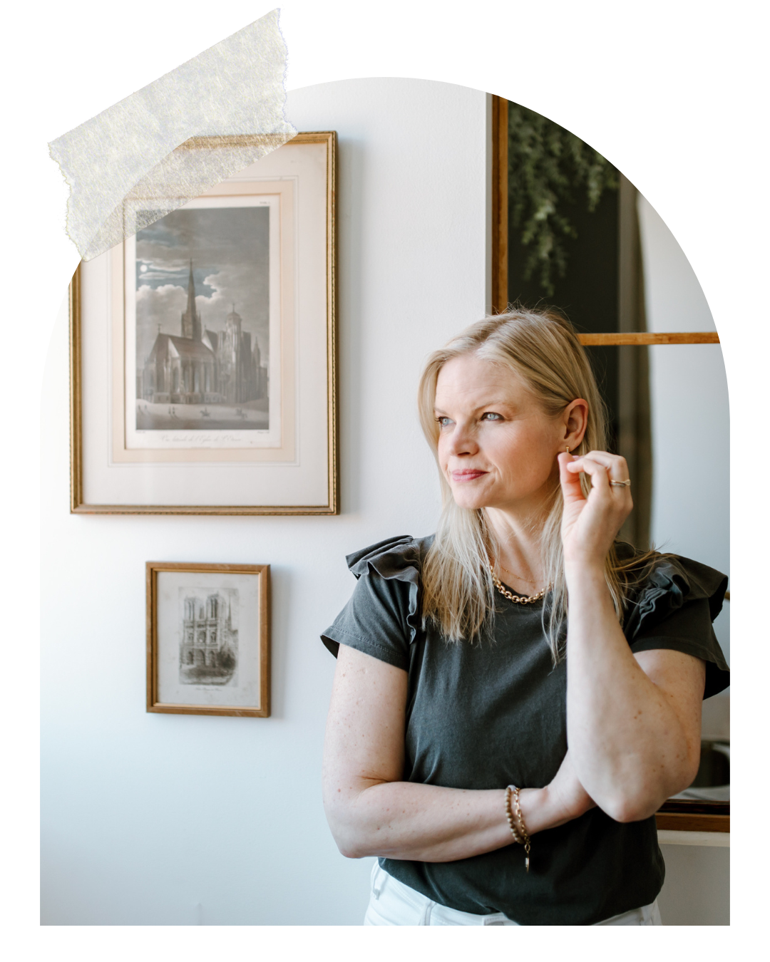 Em smirking and gazing off to the side looking out of a window, wearing a grey shirt with ruffled sleeves